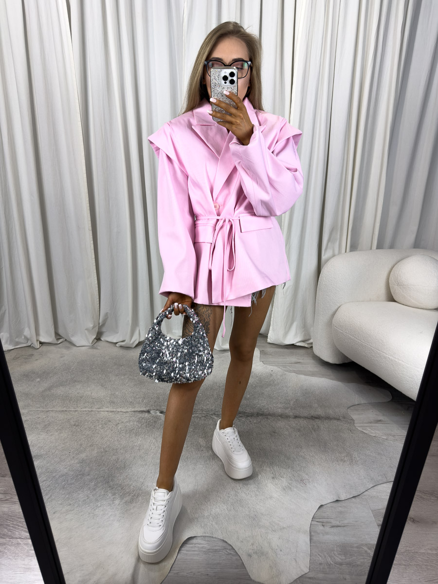 marynarka-oversize-minimal-rozowa Modelka w oversize'owej marynarce Minimal z wiązanym paskiem i szerokimi rękawami, trzymająca cekinową torebkę.
