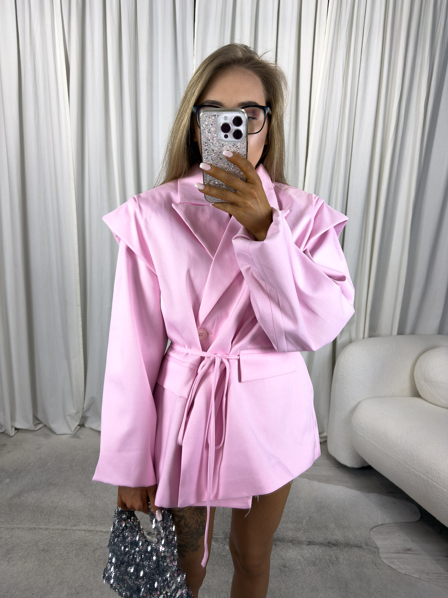 marynarka-oversize-minimal-rozowa Modelka w oversize'owej marynarce Minimal z wiązanym paskiem i szerokimi rękawami, trzymająca cekinową torebkę.